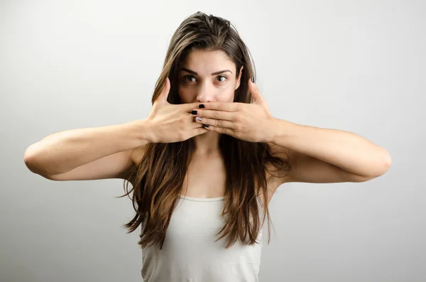 Shocking news. Surprised mature woman covering mouth with hand and staring at camera while standing against grey background