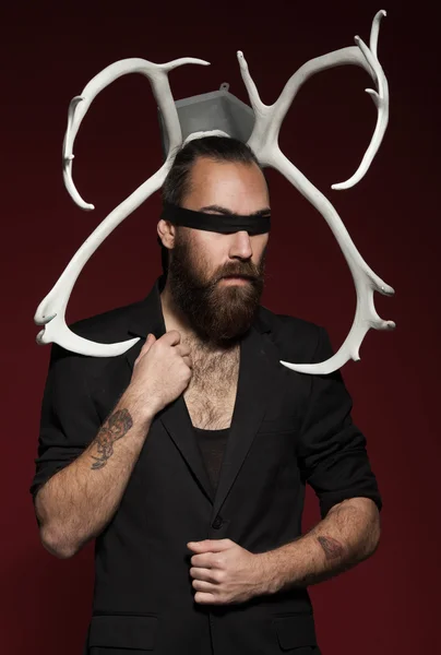 Brutal bearded man with horns. On red background. Man in black suit. fashion studio shot.