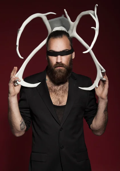 Brutal bearded man with horns. On red background. Man in black suit. fashion studio shot.