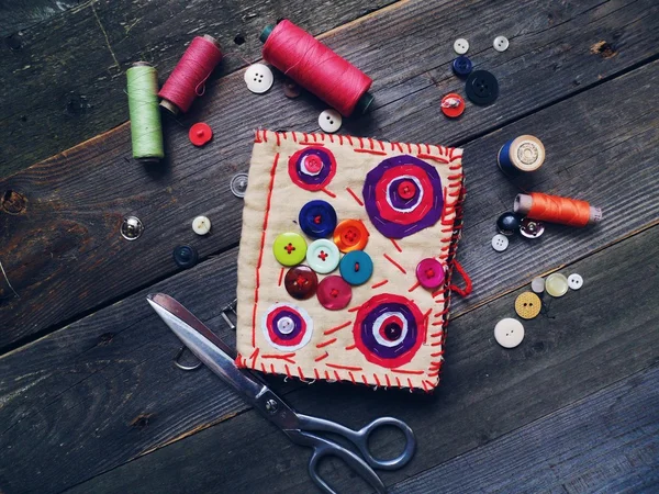 Coil colored thread, buttons, scissors, needle bed on a wooden base