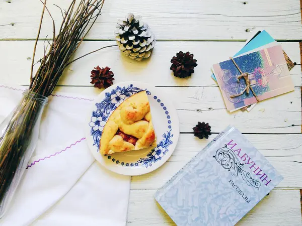 A piece of homemade cake, a book, a bunch of dry twigs and postcards