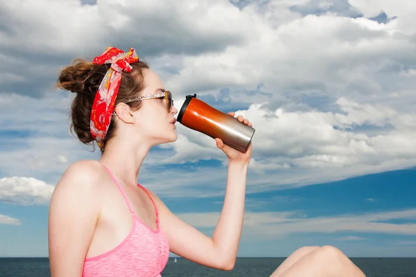 Attractive girl model drinks from metallic cup on beach