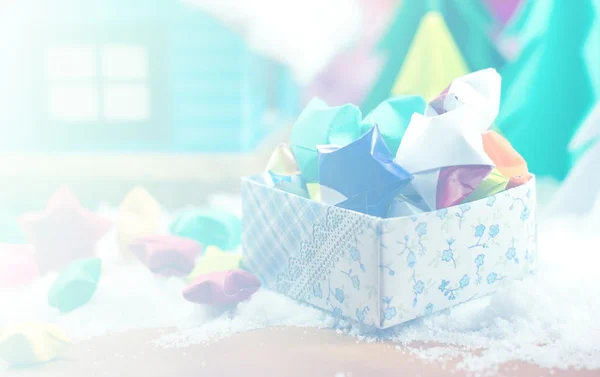 Paper stars in a gift box on the snow, with the small house and