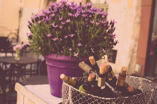 Bottles of wine with corks in an iron basket on the street with flowers, overlooking the old town of the village. retro toned background