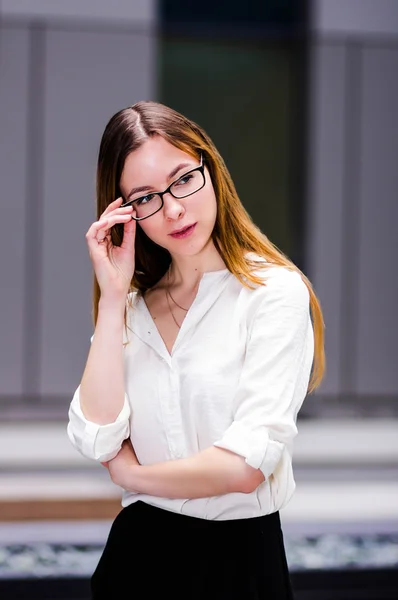 Beautiful young sexy slender and strict girl sitting holds glasses on the background of business building. portrait background