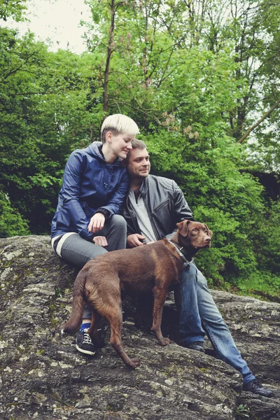 Happy family couple with dog hiking traveling in the forest on a sunny day