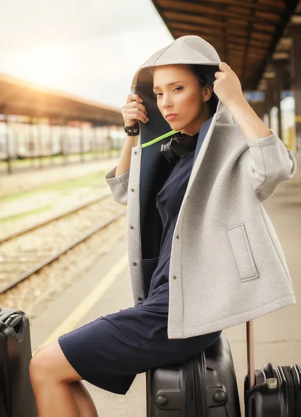 Elegant woman sitting on suitcases and waiting for the train