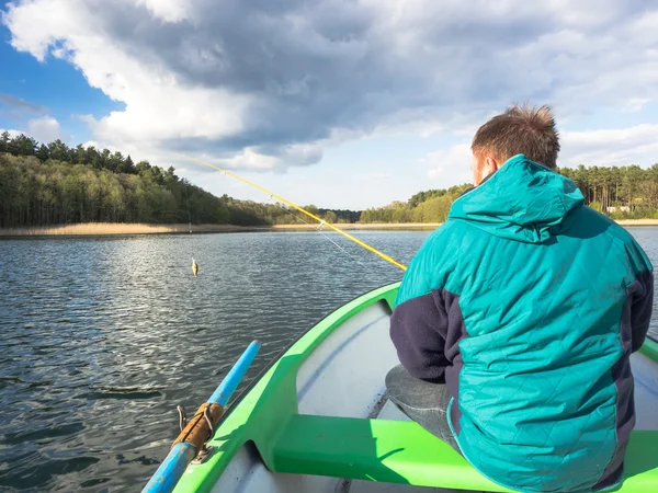 Man spending leisure time by sitting in a boat and fishing in a lake