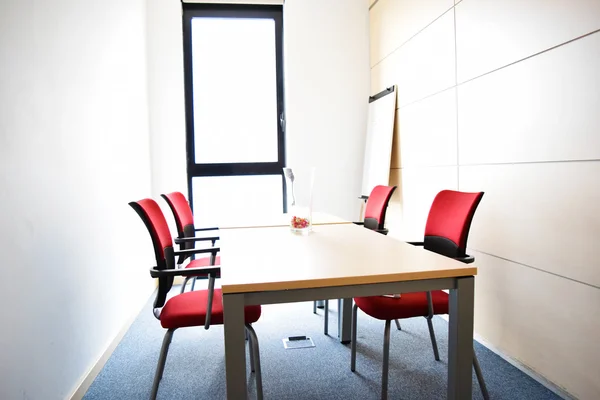 Small light empty office room with table and red chairs