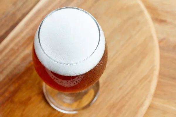 Glass of cold foamy beer on wooden background