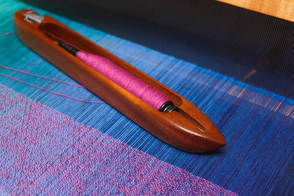 Weaving shuttle with thread on the blue warp