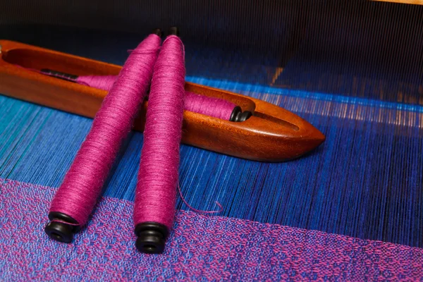 Weaving shuttle with spools of thread on the blue warp