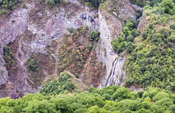 Mountain landscape waterfall flows down the cliff.