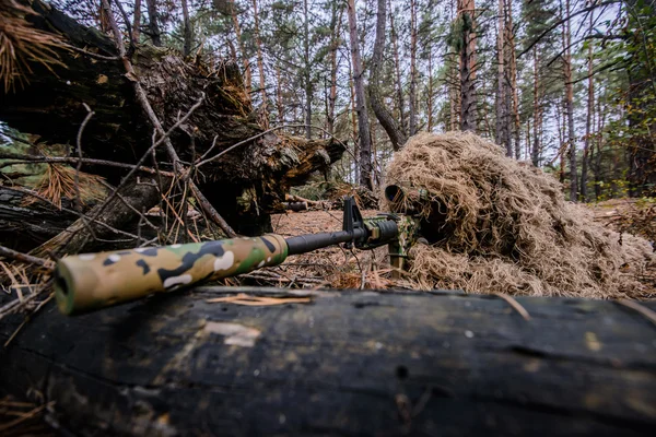 Camouflaged sniper lying in forest and aiming through his scope