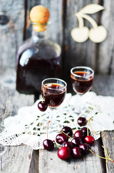 Cherry liquor in the little glasses and big bottle on the old wooden background