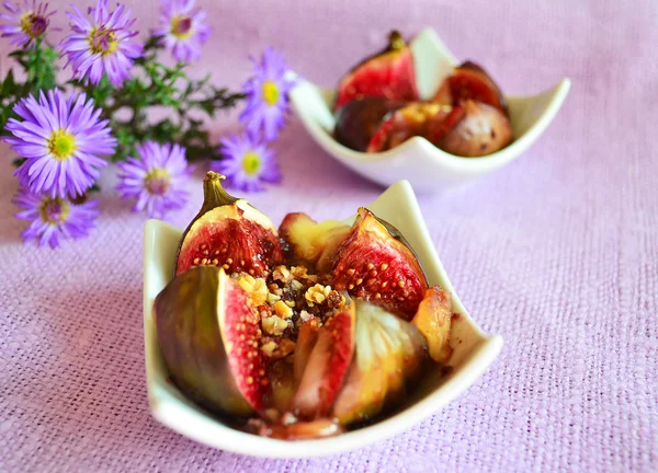 Baked figs with nuts and cheese on the purple background with purple flowers