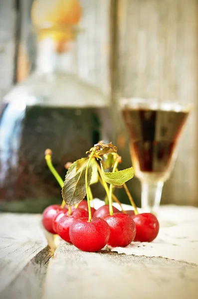 Cherry liquor in the little glasses and big bottle on the vintage napkin on the old wooden background