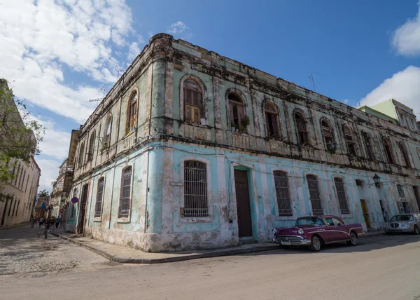 Old and colorful building in havana with pink car in front