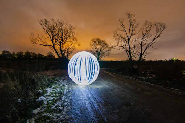 Glowing ball on spring road between two trees in a full moon