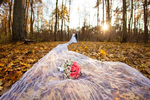 Bride and bridegroom in the autumn forest and bridal bouquet on a long bridal veil