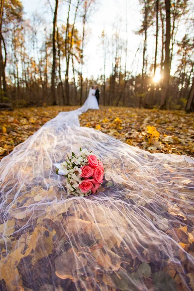 Bride and bridegroom in the autumn forest and bridal bouquet on a long bridal veil