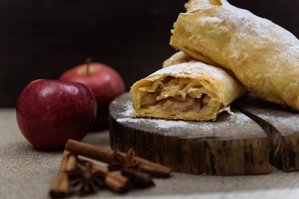 Apple strudel on wooden end of a tree with apples, cinnamon and