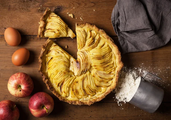 Homemade apple pie on a natural wood table with apples, eggs and flour