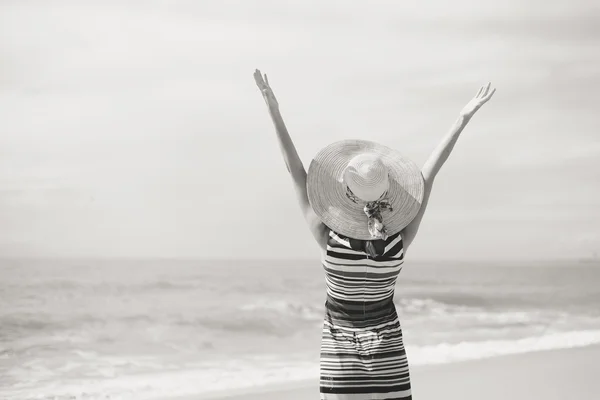 Back view of romantic lady enjoying summer beach and sun, waving at sea. Concept of feeling and freedom