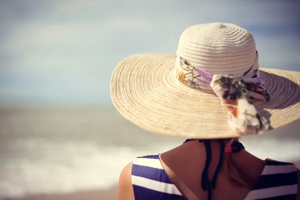 Back view of elegant beautiful woman in dress and straw hat on the beach.