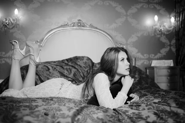 Black and white portrait of beautiful young lady relaxing lying in luxury bed