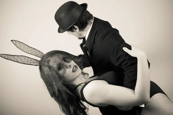 Black and white image of sexy beautiful young lady wearing bunny ears dancing with man in hat on light background