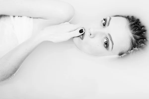 Black white photography of beautiful tender young woman touching her lips with finger lying in the water