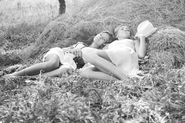 Black white photography of two happy girl friends lying on fresh hay and talking secrets closeup