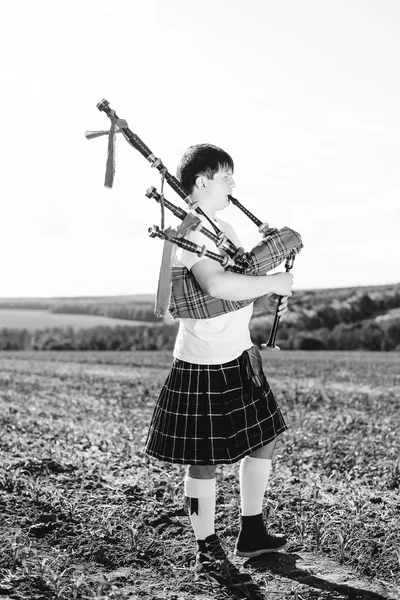 Black white photography of man enjoying playing pipes in Scottish traditional kilt on green outdoors copy space summer field