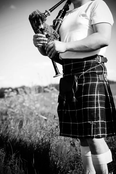 Black white photography of man enjoying playing pipes in Scottish traditional kilt on outdoors copy space summer field