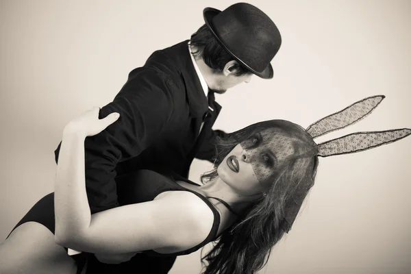 Black and white image of sexy beautiful young lady wearing bunny ears dancing with man in hat on light copy space background