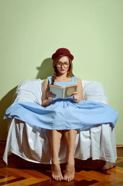 Girl in glasses and red hat sitting on the couch reading a book