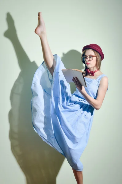 Pretty ballet dancer in a red hat and glasses reading a book
