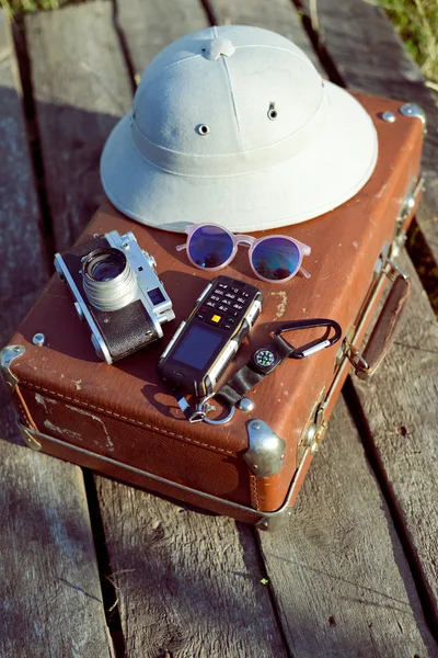 Travel background with pith helmet, camera, sunglasses and cellphone on top of retro suitcase