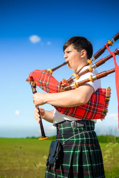 Picture of man enjoying playing pipes in Scottish traditional kilt on green outdoors summer field background copy space