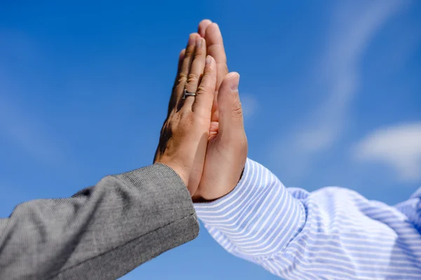 Two hands clap together under blue sky. Business man and woman giving five, hands detail.