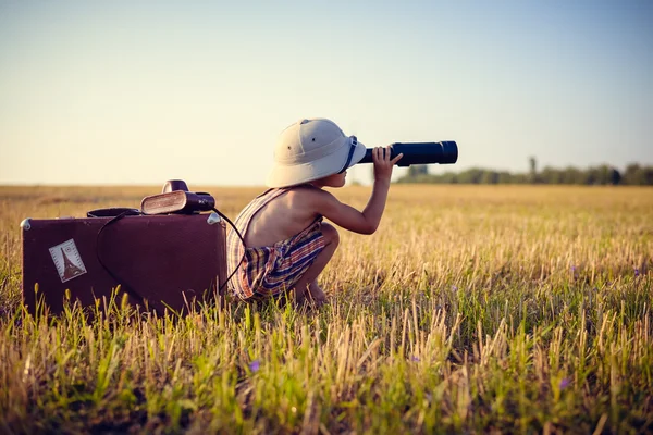 Little boy looking in spyglass on sunny field countryside background.