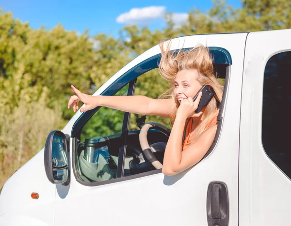 Picture of blond girl in white car speaking by phone and looking from car window and pointing up