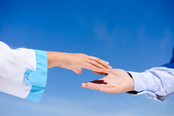 Handshake between a man and a doctor over blue sky on sunny day outdoors background, closeup picture