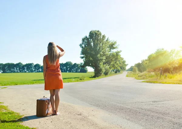 Young woman with suitcase looking at distance on country crossroad