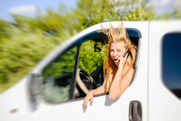 Image of excited pretty girl speaking phone and looking from car window on sunny countryside.