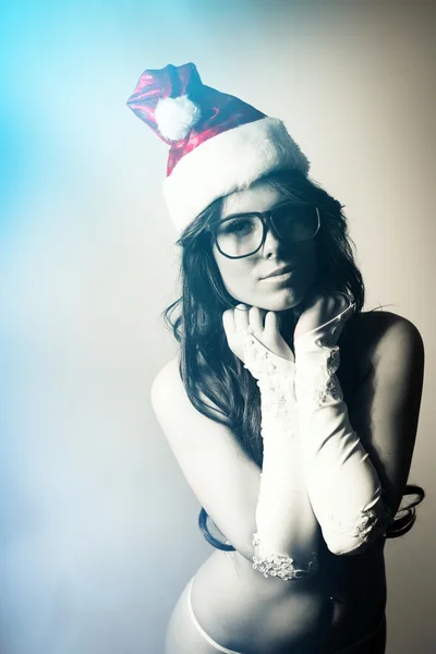 Picture of looking at camera through hipster glasses pretty young lady with perfect body in white sexual lingerie and red santa claus hat