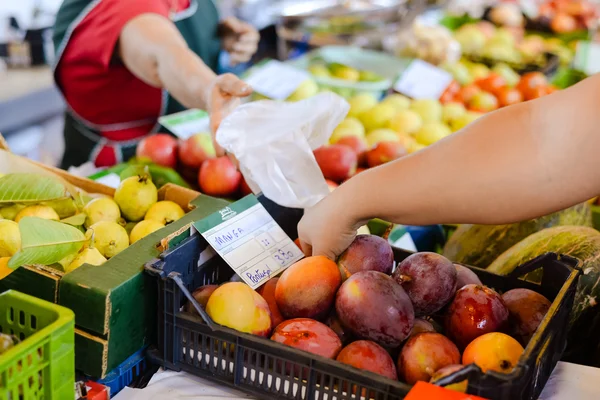 Buyers hand taking mango beside price tag in colorful marketplace