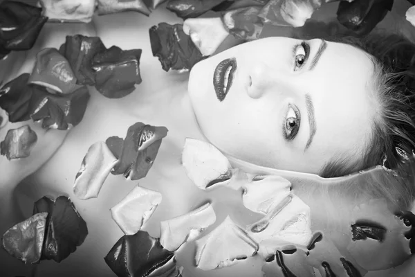 Beautiful young lady relaxing laying in water bath and looking at camera on rose flower petals copy space background close up portrait