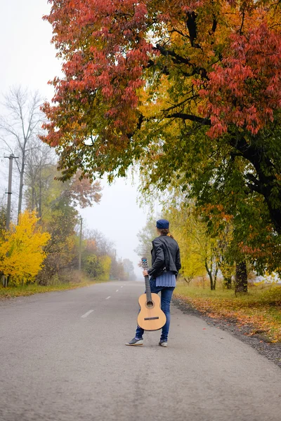 Beautiful young lady in jeans with guitar on countryside road